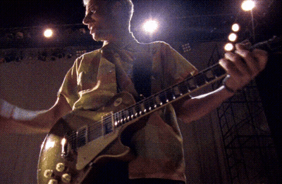 A Man In A Yellow Shirt Is Playing A Guitar In A Dark Room GIF