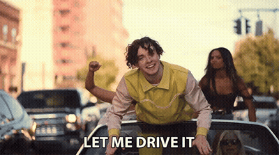 A Man In A Yellow Shirt Is Riding In The Back Of A Car With The Words Let Me Drive It Written Below Him . GIF