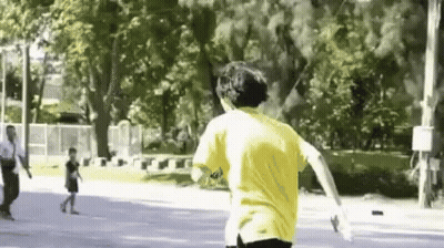 A Man In A Yellow Shirt Is Running Down A Street In A Park . GIF