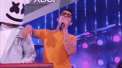 A Man In A Yellow Shirt Is Singing Into A Microphone While A Man In A White Jacket Is Playing A Keyboard . GIF