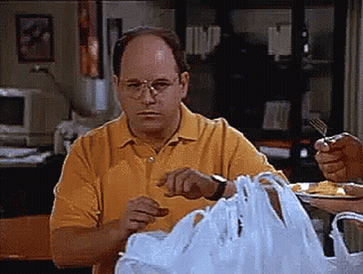 A Man In A Yellow Shirt Is Sitting At A Table With A Plastic Bag In Front Of Him GIF