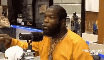 A Man In A Yellow Shirt Is Sitting In Front Of A Microphone And Talking Into It . GIF