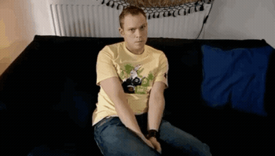 A Man In A Yellow Shirt Is Sitting On A Black Couch GIF