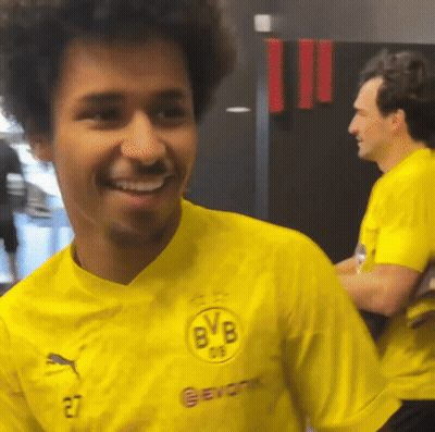 A Man In A Yellow Shirt Is Smiling In A Room . GIF