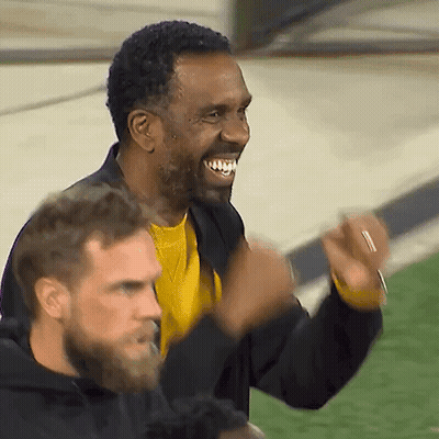 A Man In A Yellow Shirt Is Smiling While Another Man In A Black Jacket Looks On GIF