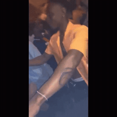 A Man In A Yellow Shirt Is Smoking A Cigarette In A Dark Room GIF