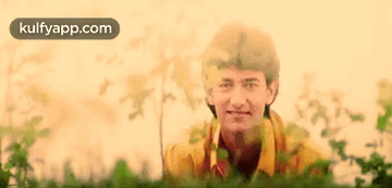 A Man In A Yellow Shirt Is Standing In A Field Of Grass . GIF