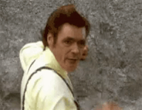 A Man In A Yellow Shirt Is Standing In Front Of A Gray Wall . GIF