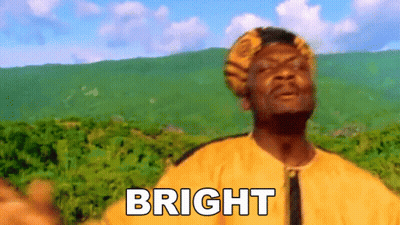 A Man In A Yellow Shirt Is Standing In Front Of A Mountain With The Word Bright Written On His Chest . GIF