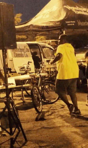 A Man In A Yellow Shirt Is Standing In Front Of A Van That Says Daniels On It GIF