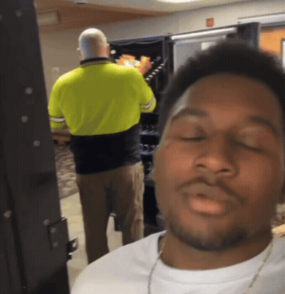 A Man In A Yellow Shirt Is Standing In Front Of A Vending Machine With His Eyes Closed GIF