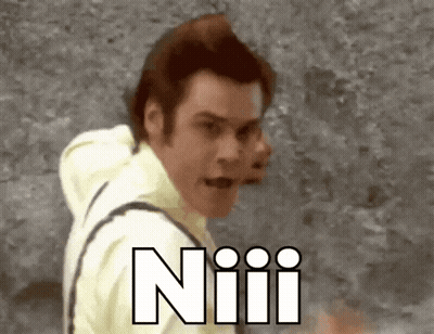 A Man In A Yellow Shirt Is Standing In Front Of A Wall With The Word Niiii Written In White GIF
