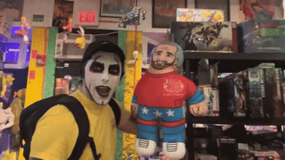 A Man In A Yellow Shirt Is Standing Next To A Stuffed Wrestler GIF
