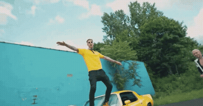 A Man In A Yellow Shirt Is Standing On A Car GIF