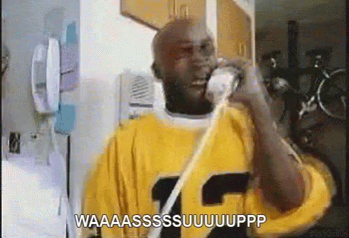 A Man In A Yellow Shirt Is Talking On A Phone And Says Waaaassssuuuuupp GIF