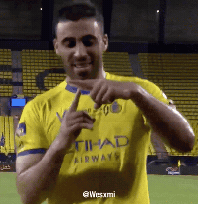 A Man In A Yellow Shirt That Says Etihad Airways Is Pointing GIF
