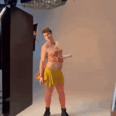 A Man In A Yellow Skirt And Top Is Standing In A Room . GIF