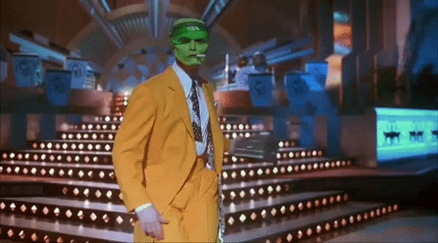A Man In A Yellow Suit And Green Mask Is Standing On A Stage GIF