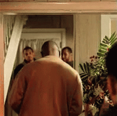 A Man In A Yellow Sweater Is Standing In A Doorway With A Group Of People Behind Him . GIF