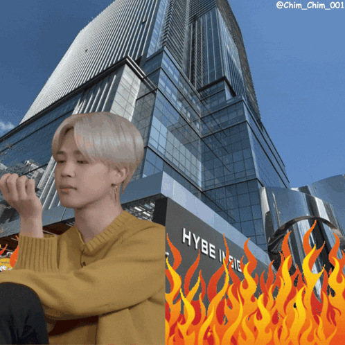 A Man In A Yellow Sweater Sits In Front Of A Building That Says Hybe Indie GIF
