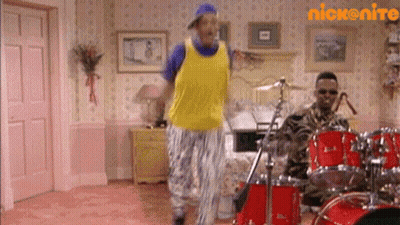 A Man In A Yellow Tank Top Is Dancing In Front Of A Drum Set In A Room . GIF