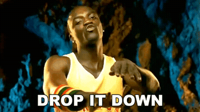 A Man In A Yellow Tank Top Is Pointing At The Camera With The Words Drop It Down Written Below Him GIF