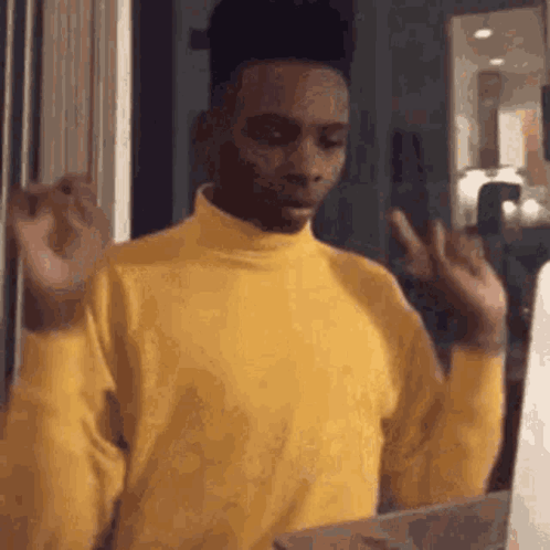 A Man In A Yellow Turtleneck Sweater Is Making A Funny Face While Holding A Box . GIF