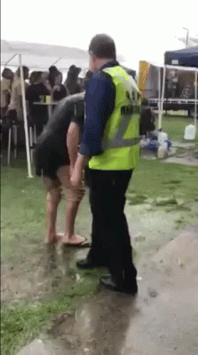A Man In A Yellow Vest Is Standing Next To A Woman In A Black Dress . GIF