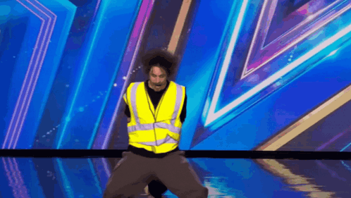 A Man In A Yellow Vest Is Standing On A Stage GIF