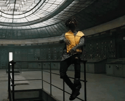 A Man In A Yellow Vest Sits On A Railing In An Empty Room GIF