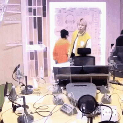 A Man In A Yellow Vest Stands In Front Of A Microphone In A Room GIF