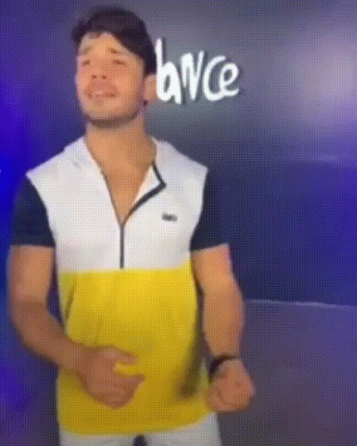A Man In A Yellow White And Black Shirt Is Dancing In Front Of A Sign That Says Dance GIF