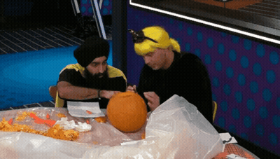 A Man In A Yellow Wig Is Carving A Pumpkin With Another Man GIF