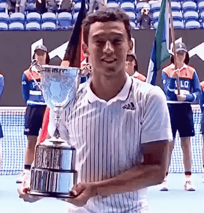 A Man In An Adidas Shirt Is Holding A Trophy On A Tennis Court GIF