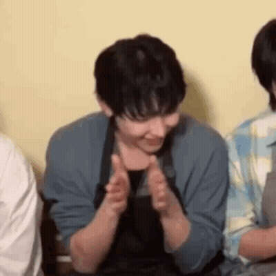 A Man In An Apron Is Clapping His Hands While Sitting Next To A Group Of People . GIF