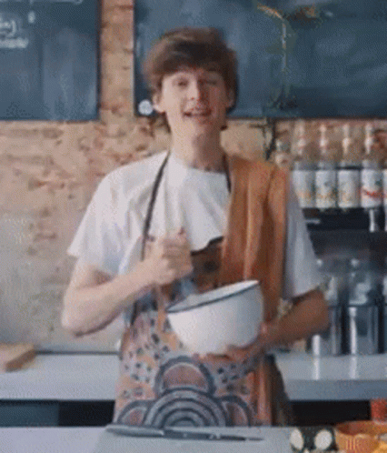 A Man In An Apron Is Holding A Bowl In His Hands . GIF