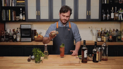A Man In An Apron Is Preparing A Drink In A Kitchen With Many Bottles GIF