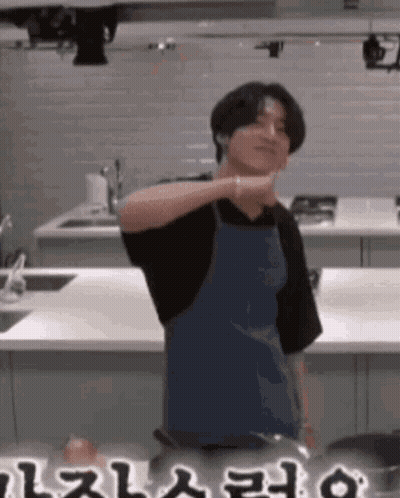 A Man In An Apron Is Standing In A Kitchen With A Pot . GIF