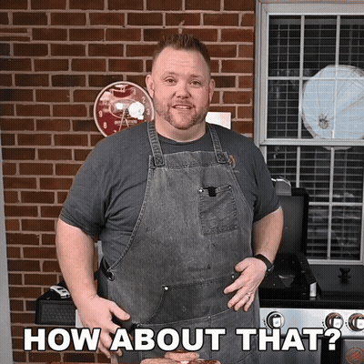 A Man In An Apron Says How About That In Front Of A Brick Wall GIF