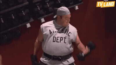 A Man In An Athletic Dept Shirt Is Lifting Dumbbells In A Gym GIF