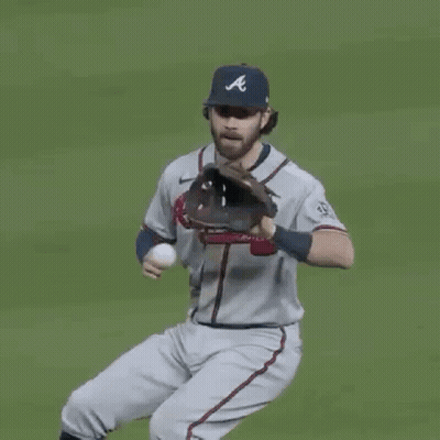 A Man In An Atlanta Braves Jersey Is Standing On A Baseball Field And Smiling . GIF