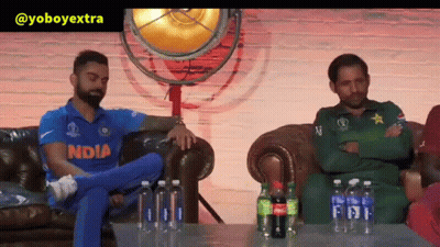 A Man In An India Jersey Sits On A Couch Next To A Man In A Green Uniform GIF