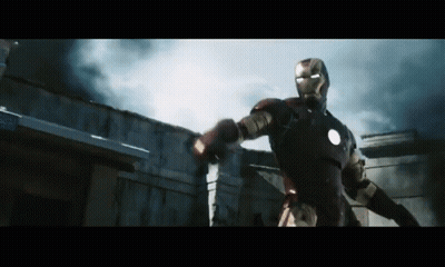 A Man In An Iron Man Suit Is Standing In Front Of A Building With Smoke Coming Out Of It GIF