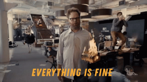 A Man In An Office Holding A Burning Piece Of Wood With The Words Everything Is Fine Behind Him GIF