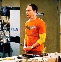 A Man In An Orange Batman Shirt Stands In Front Of A Door GIF