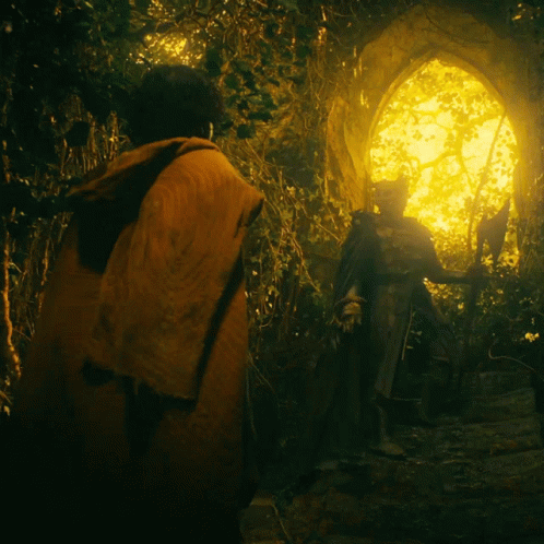 A Man In An Orange Cape Stands In Front Of A Statue In A Dark Forest GIF