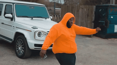 A Man In An Orange Hoodie Is Standing In Front Of A White Jeep GIF