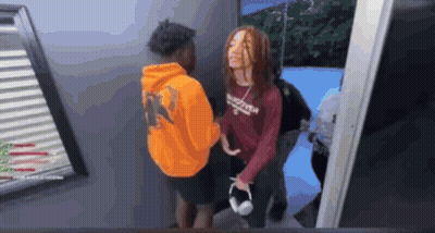 A Man In An Orange Hoodie Is Standing Next To A Woman In A Red Shirt With The Word Supreme On It GIF