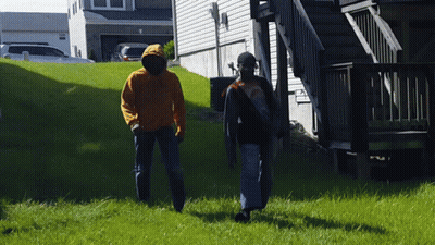 A Man In An Orange Hoodie Walks With Another Man GIF