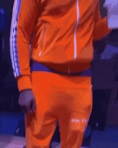 A Man In An Orange Jacket And Orange Sweatpants Is Standing On A Stage GIF